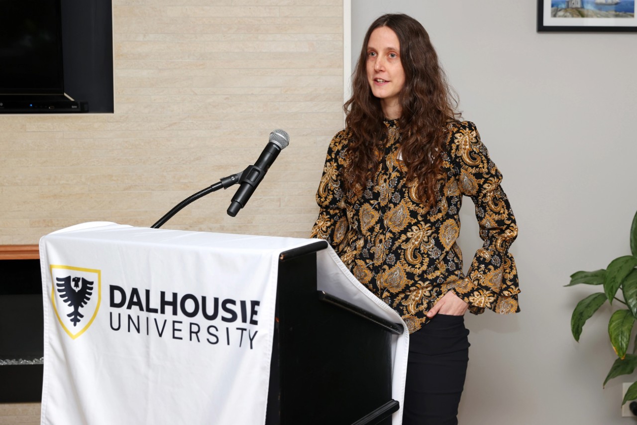 Crystal Parker standing with one hand in her pocket as she speaks into a microphone at the podium during the event. 