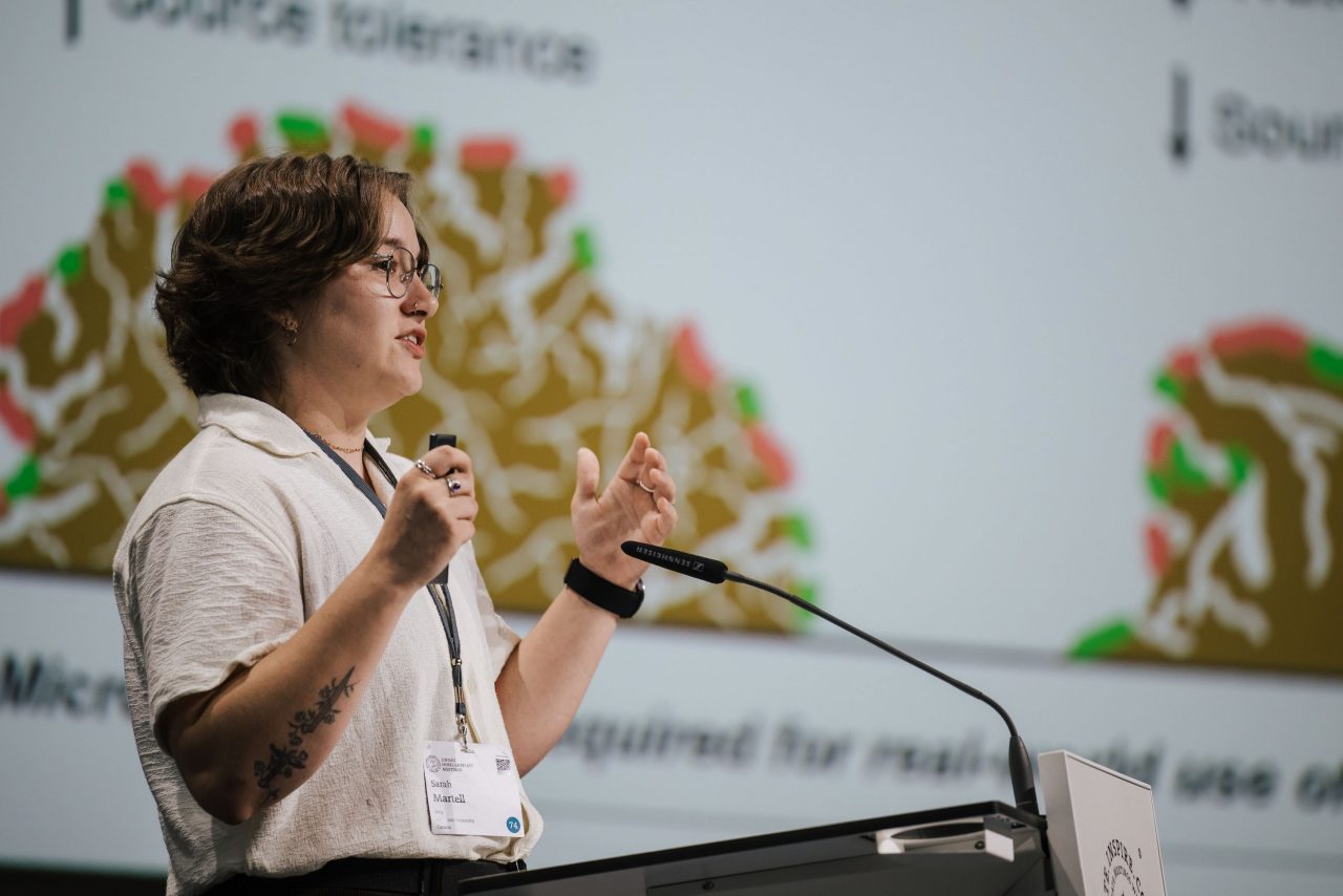 Martell on stage at a podium speaking into a microphone and gesturing with her hands.