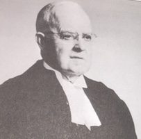 A black and white archival photo of a man in judge's robe.