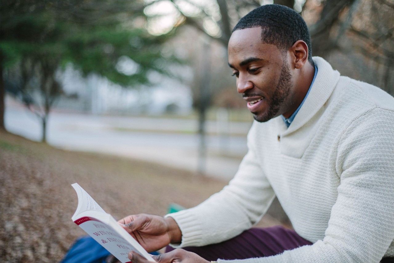 Man in white sweater reading a book outside