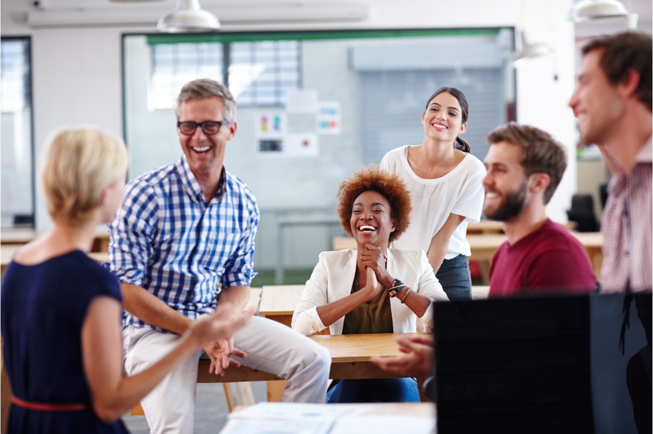 A group of people sitting and standing in an office space smiling and laughing