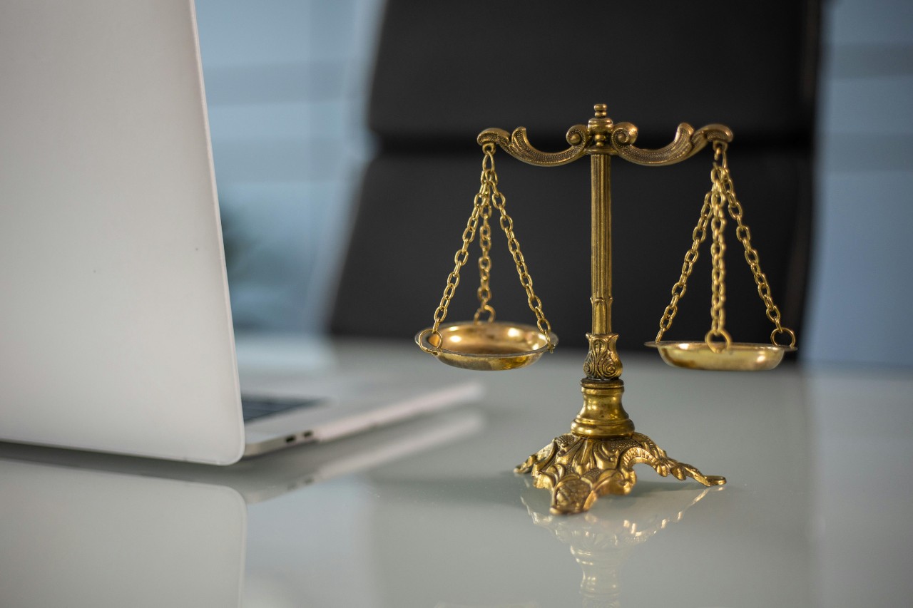 A gold statue of the scales of justice sits on a desk next to a laptop