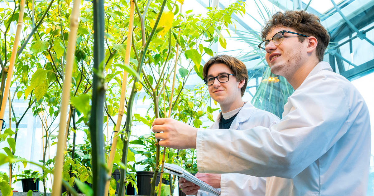 Two students in lab coats in a greenhouse
