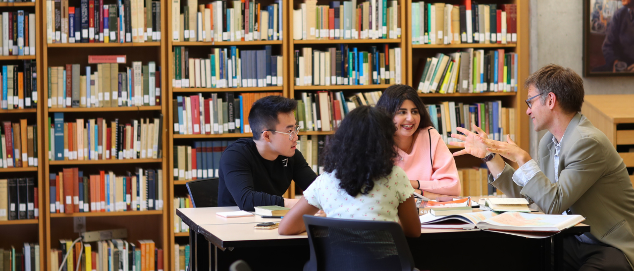 Group of students sitting around a table talking with professor in library