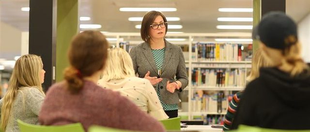 Professor lecturing to a few sitting students in a library