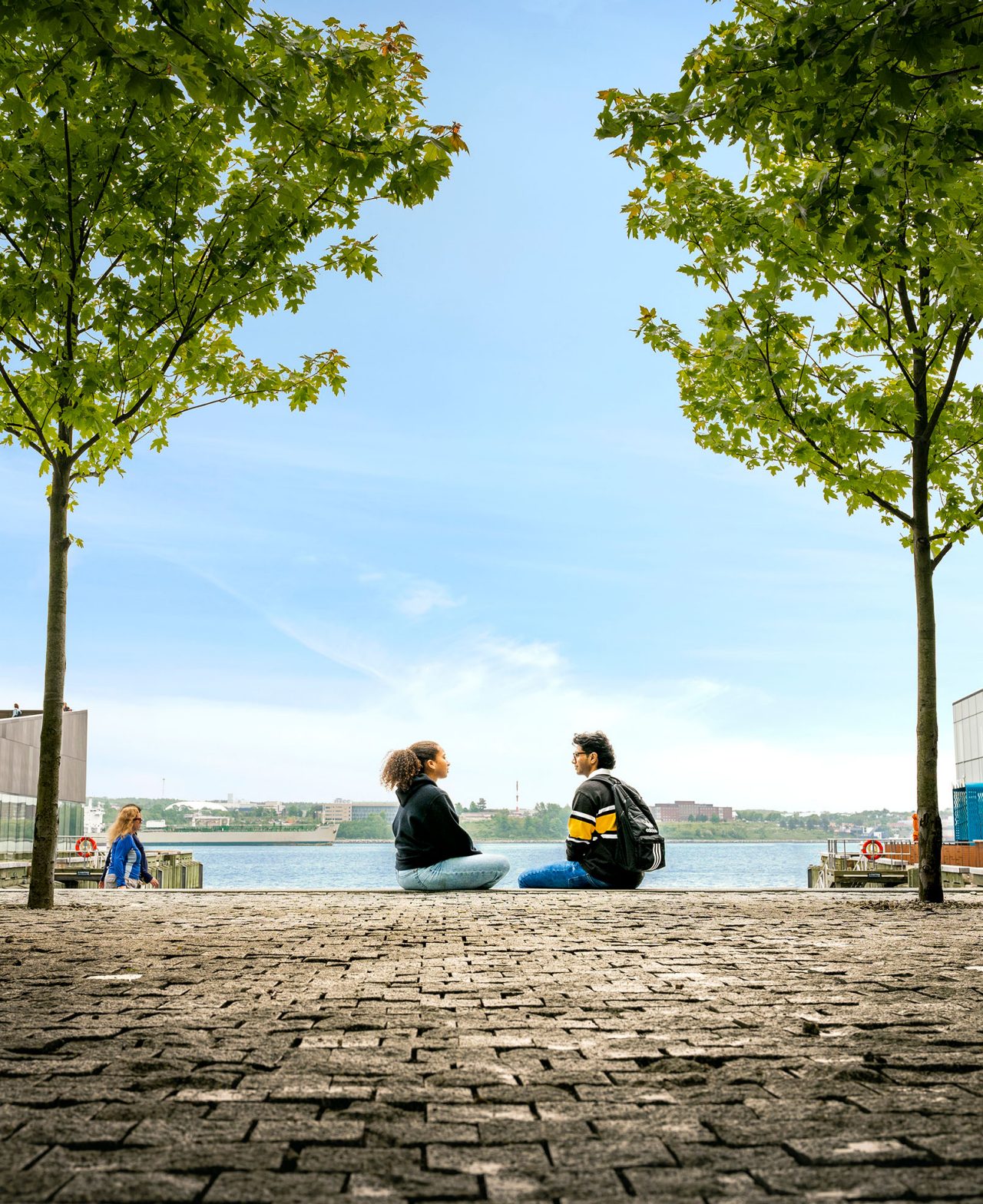 Students sit on cobbled courtyard facing each other with Halifax harbour in the background.