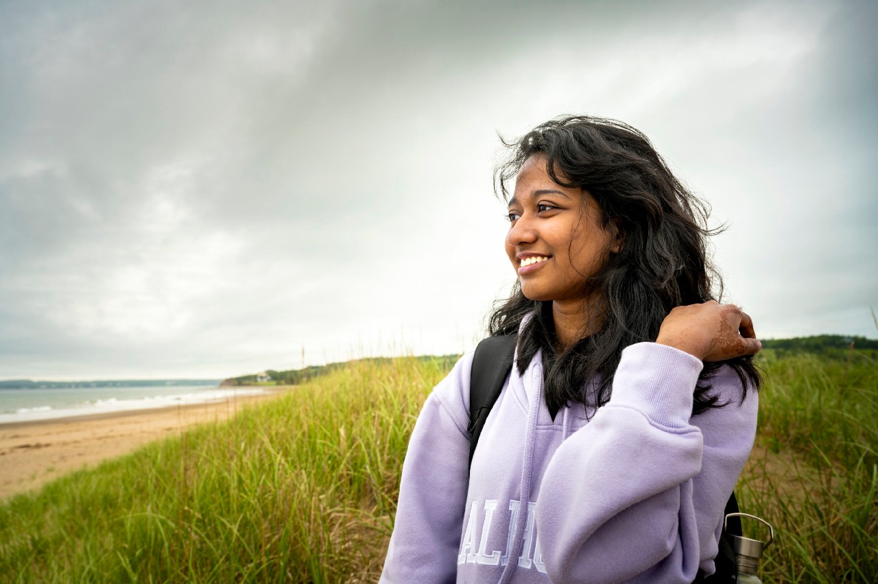 A Dal student stands on grassy area by the beach looking out at the ocean