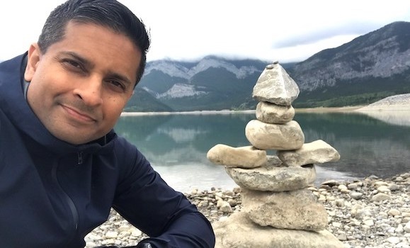 Man in front of lake and mountains with stone sculpture.