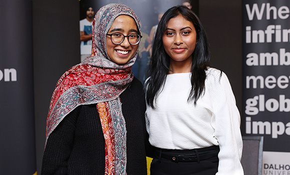 Two women stand side-by-side in front of Dal banners.