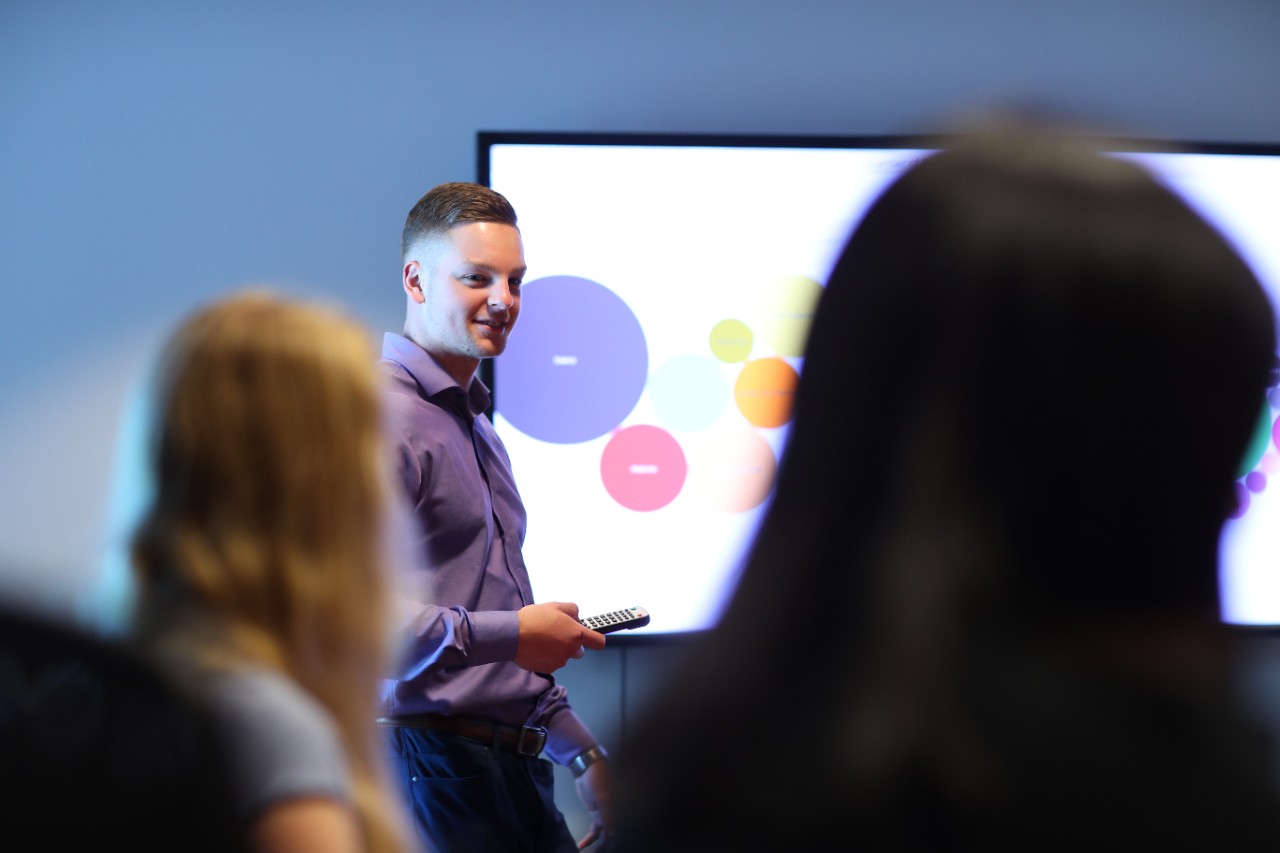 A student with short hair is standing at a large screen displaying an infographic with different colour circles.