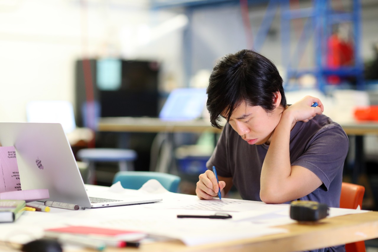 A person with medium length black hair uses a pen to write on pieces of paper.