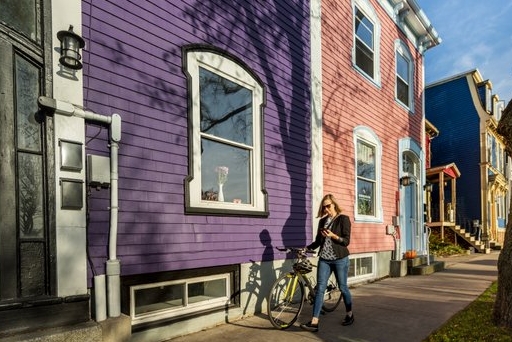 A person walking on a sidewalk past a purple and pink house.