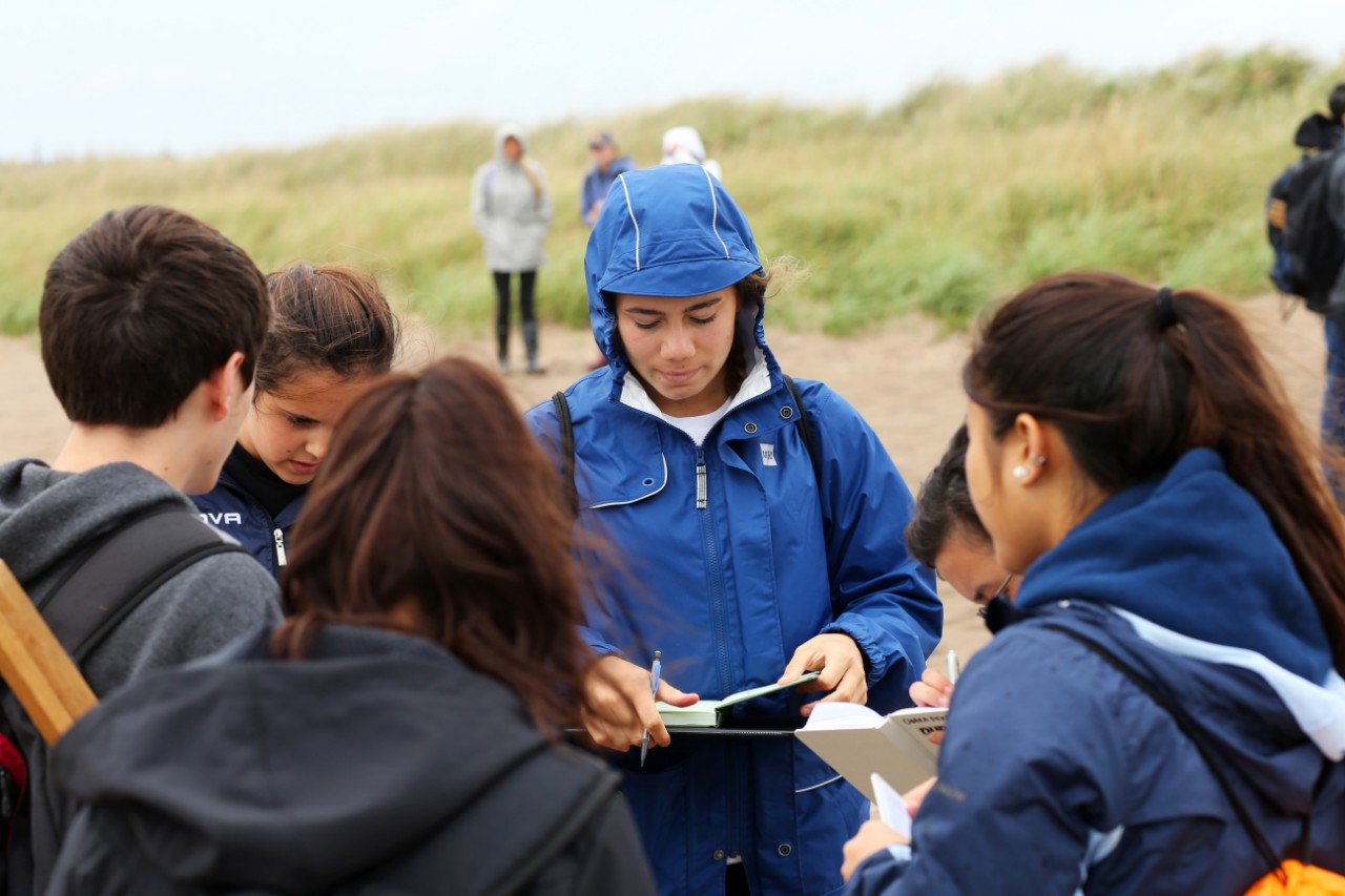 Science students stand in a group and review their notes while they attend a field trip at Conrad's Beach, Nova Scotia