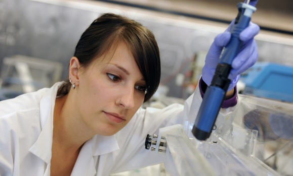 A researcher wearing a lab coat prepares to look at a microscope