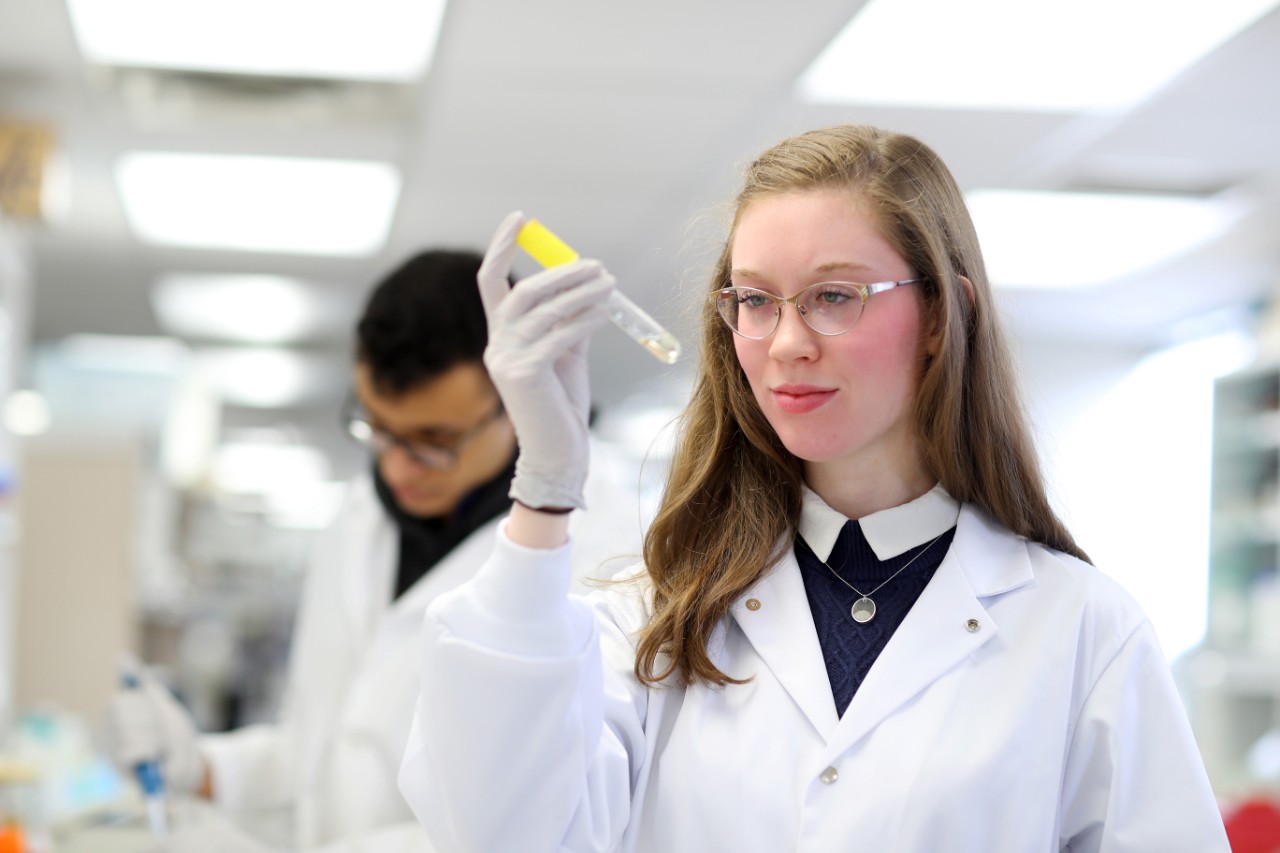 A student observes a sample in a test tube while they conduct research in a lab