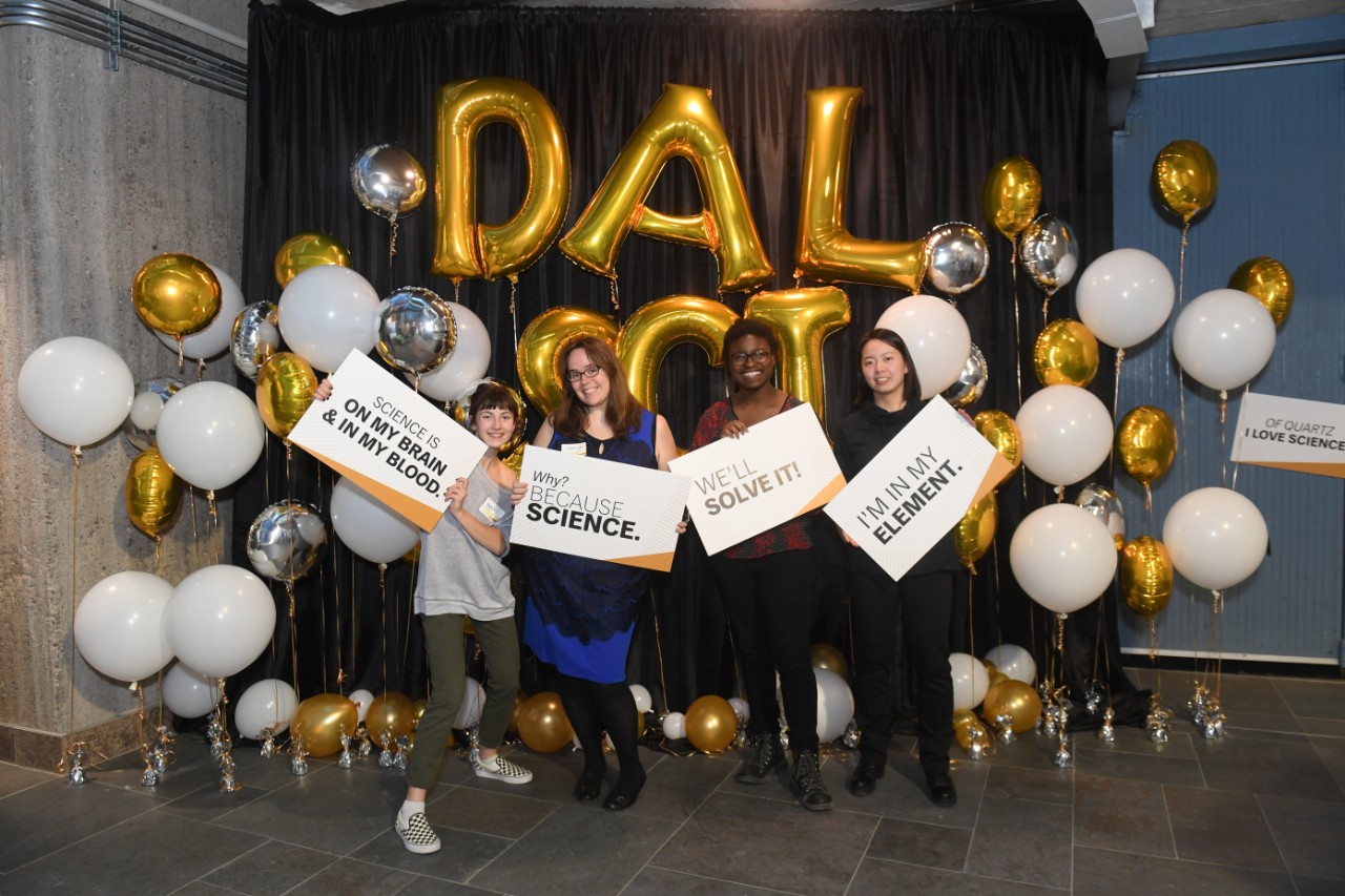 Students and faculty hold up signs and pose for a photo while they attend the Dalhousie Science Deans Reception