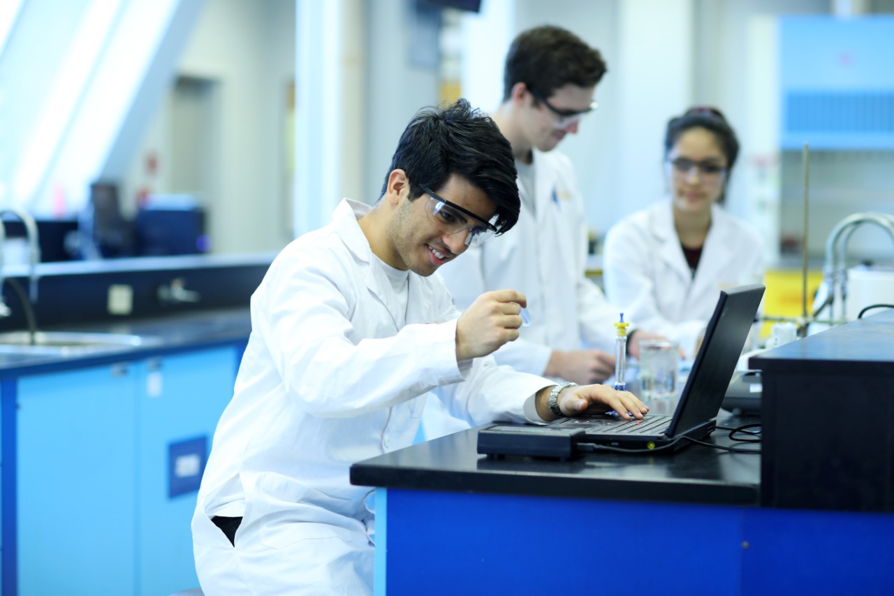 Undergraduate science student works on a lab report while other students talk in the background