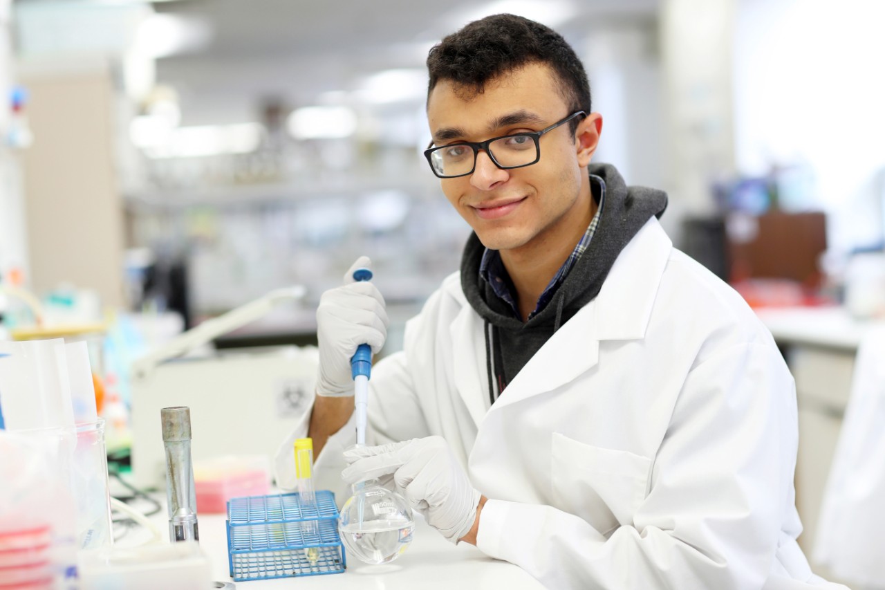 A Dalhousie science student in a white lab coat sits at a lab bench and conducts research