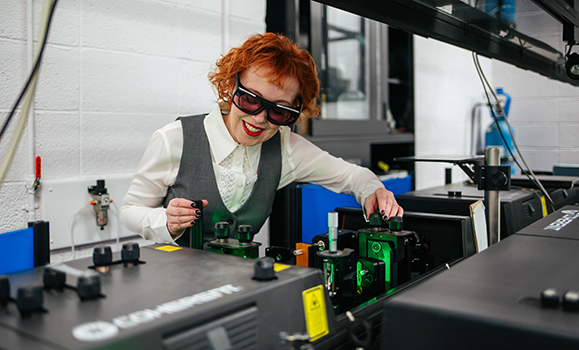 A researcher wearing protective goggles works in a lab space