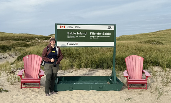 A students stands by a Sable Island sign during a research visit