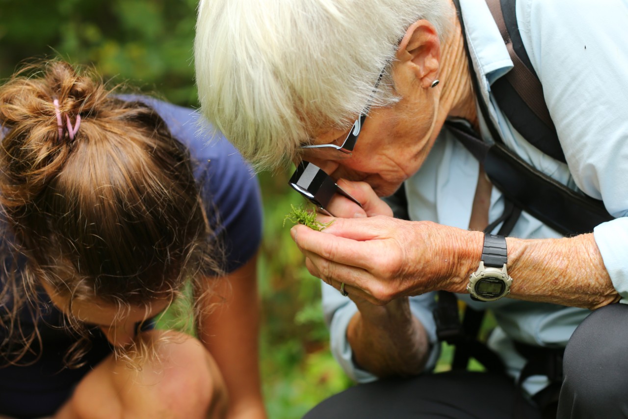 A researcher and a student look closely at a soil sample outdoors