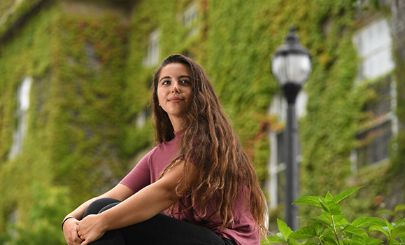 A student sits in front of a building with green vines
