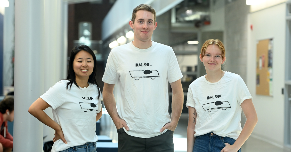Three people standing together wearing white t-shirts that have a drawing of a solar car on them