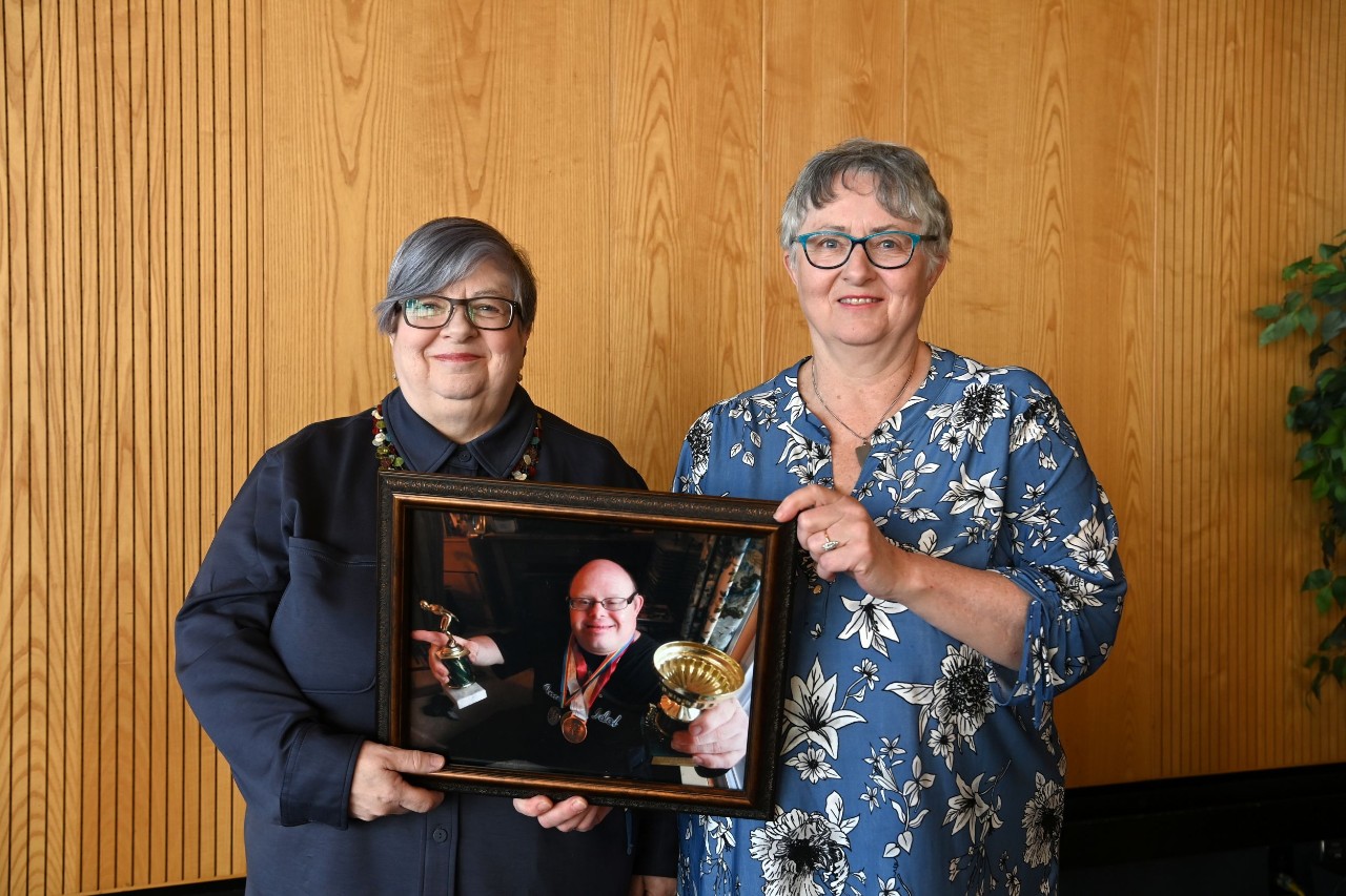 Two women hold a framed photo of their brother.