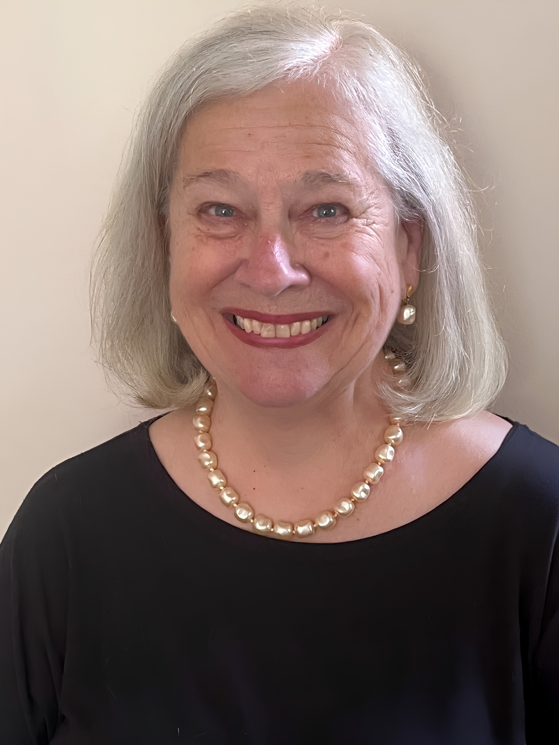 A white-haired woman wearing a black shirt and a pearl necklace