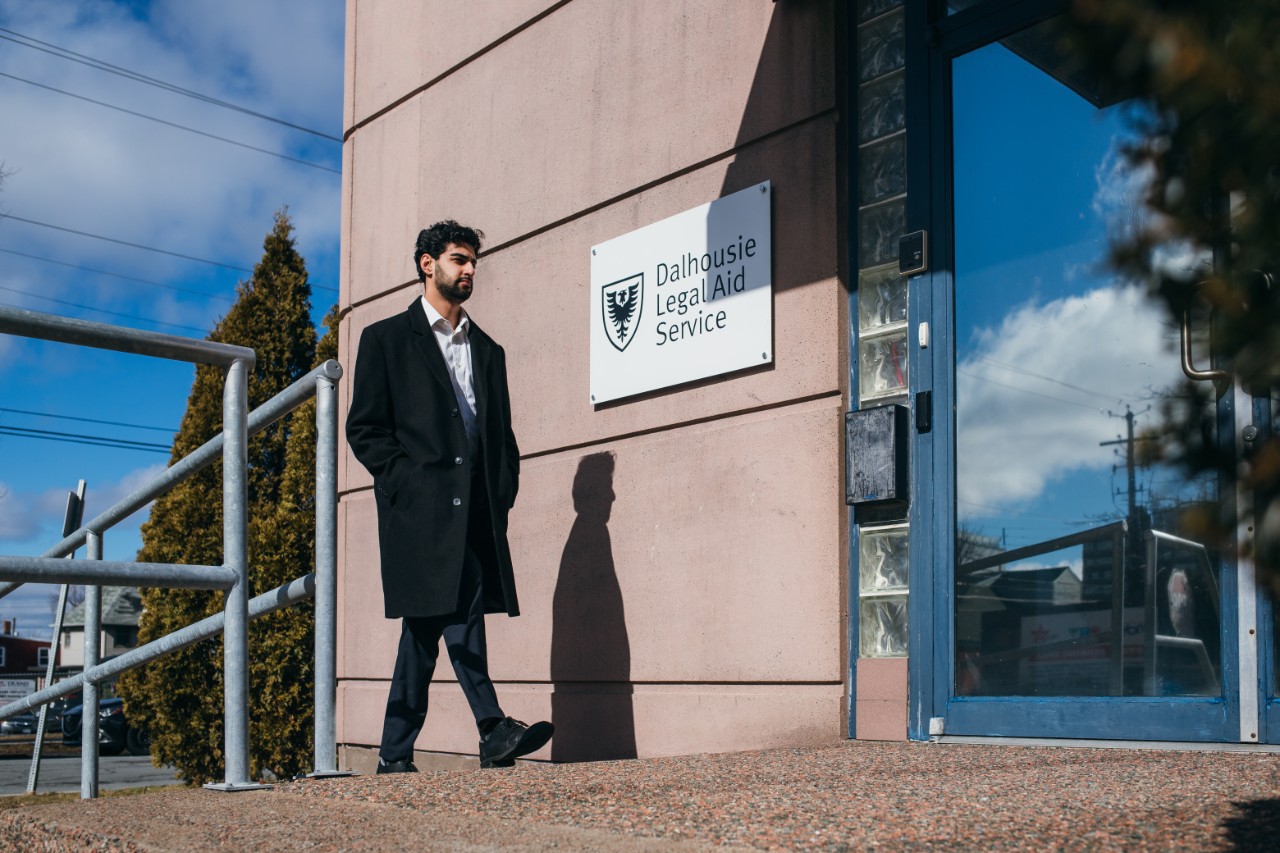 A man in a black coat walking toward a building with the sign Dalhousie Legal Aid Service on the outside