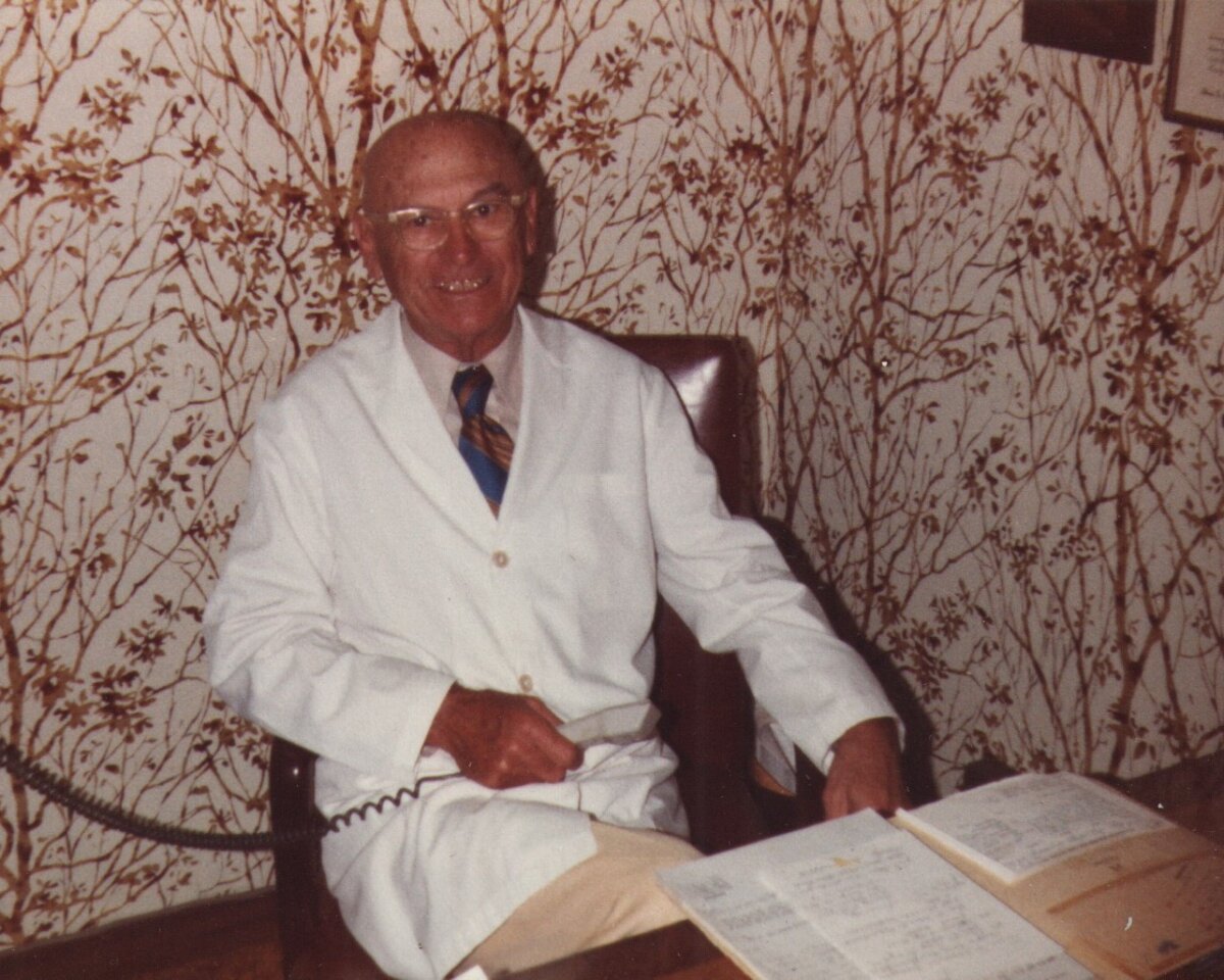 A man in a white doctor's coat seated at a table holding a piece of medical equipment