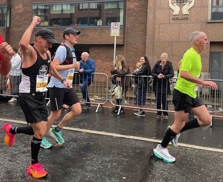 Three men running in a marathon, one celebrates by pumping his fist in the air.