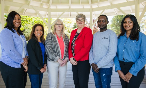 A group of six people standing and smiling in a row under a gazebo outdoors.