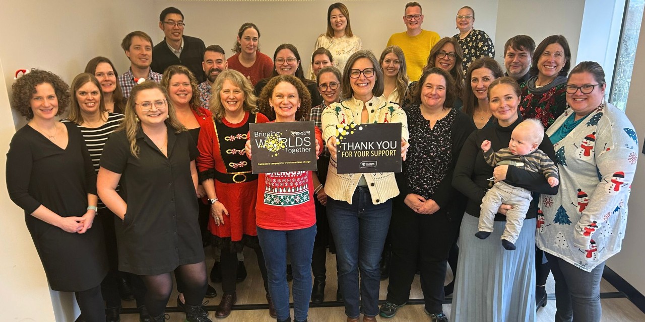 A group of people smiling, some wearing holiday attire, gathered at an event.