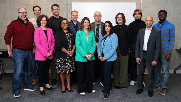 A group of people stand together in a classroom space at a celebration.