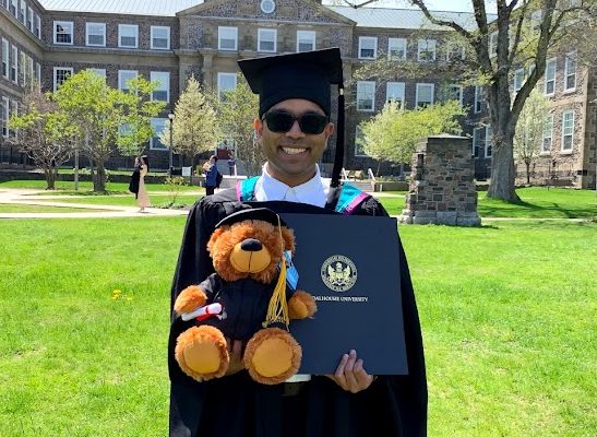 A man wearing graduate robes and holding a teddy bear and degree