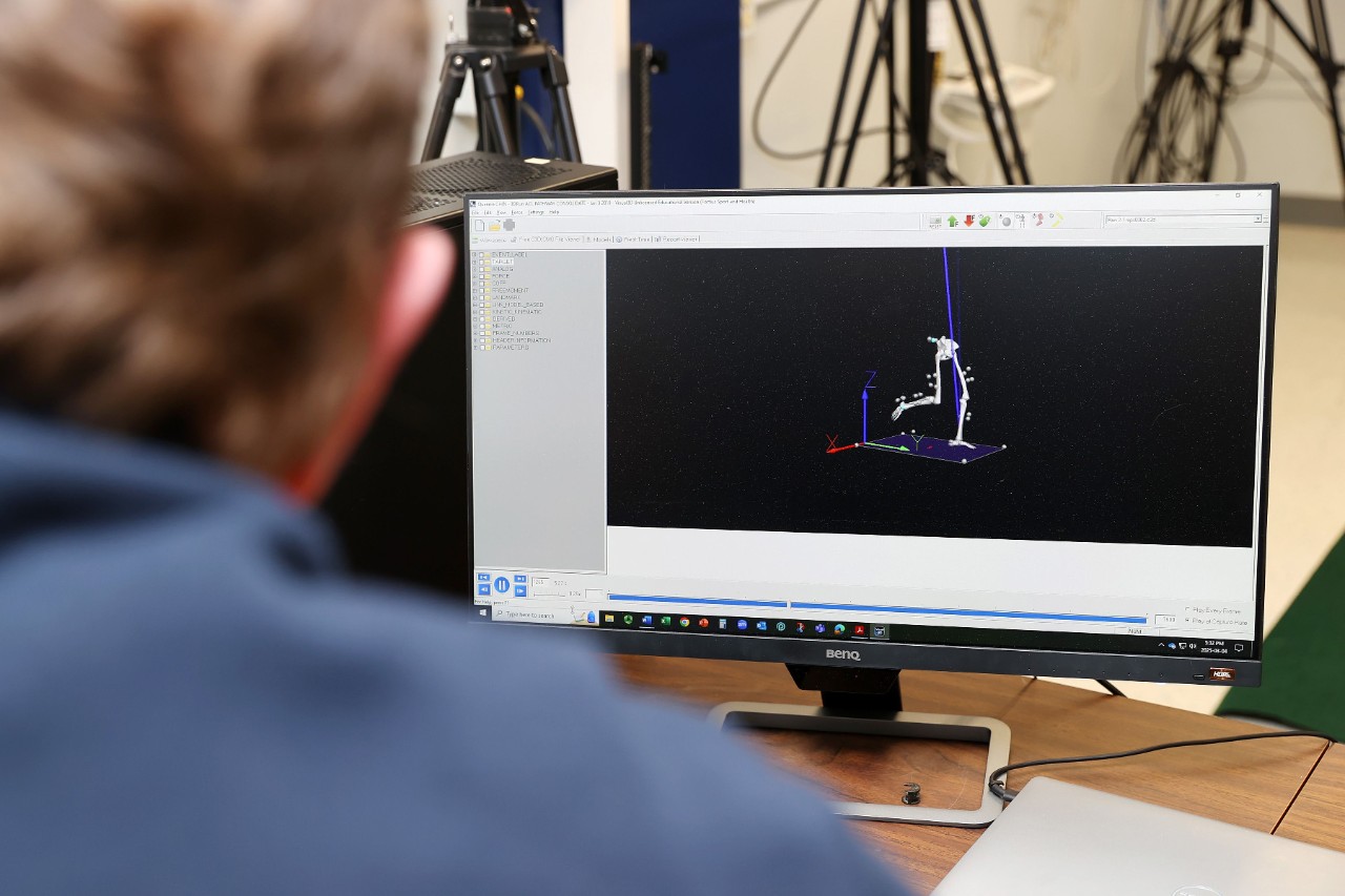 An individual in a blue shirt is looking at a computer monitor that is displaying motion capture data