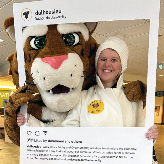 Galarneau standing next to the Dalhousie tiger indoors and holding up a large social media photo frame.