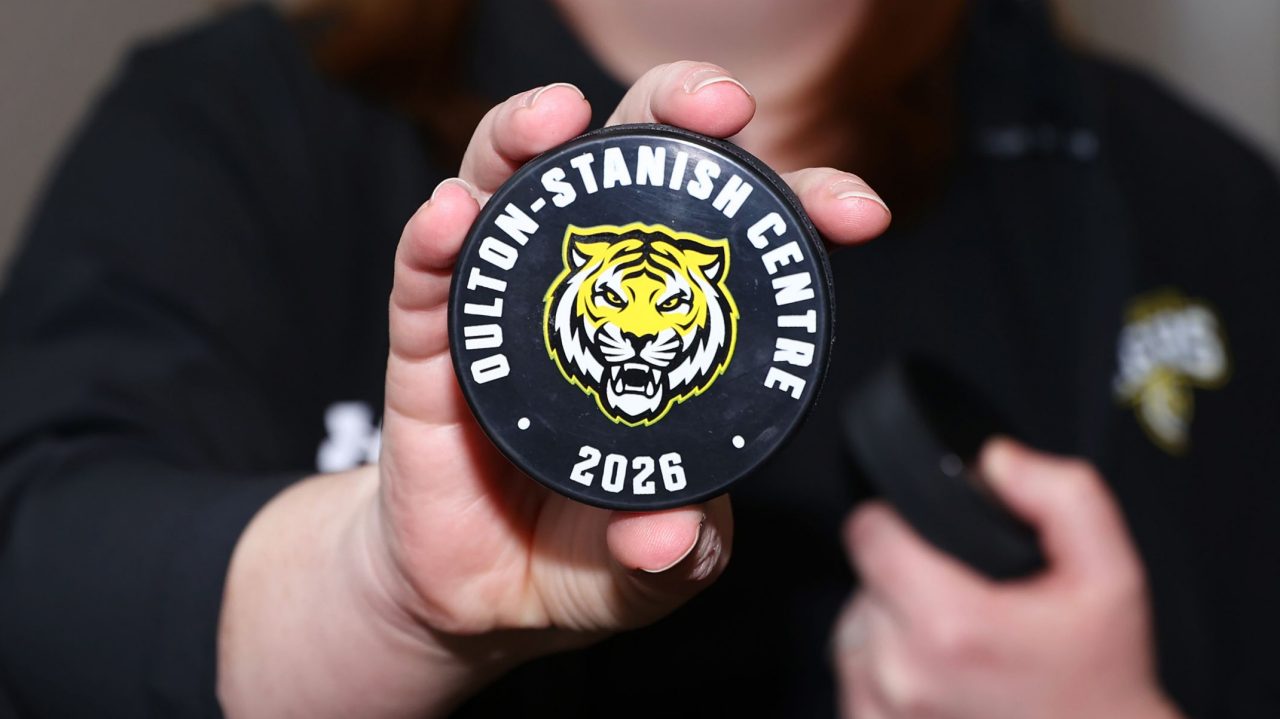 A person holds a hockey puck with a tiger face in focus while their torso is blurred in the background.