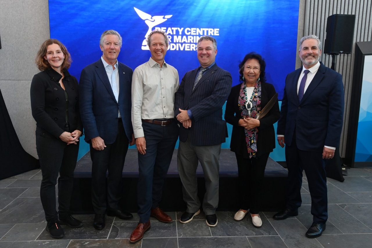 A group of six men and women standing together, smiling at an event.