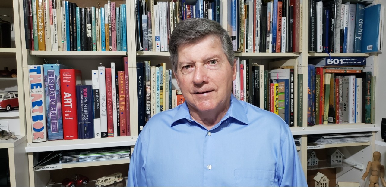 Daniel Parent stands in front of a book shelf filled with architecture and art related books.