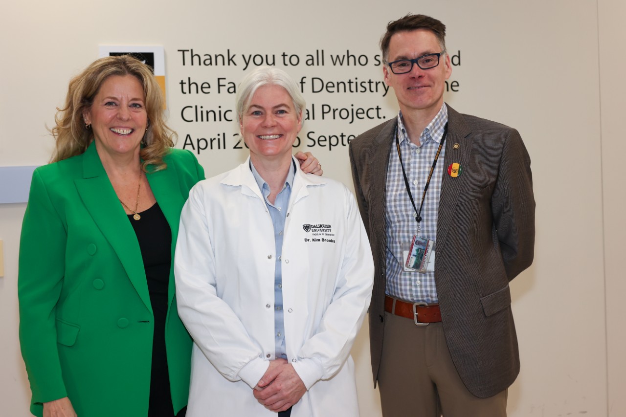 A woman wearing a green blazer poses with a woman wearing a white lab coat and a man wearing a grey suit