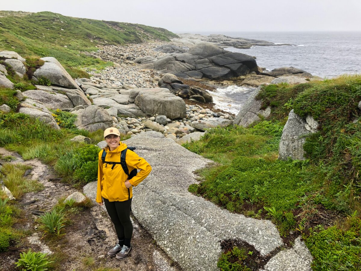 A woman wearing a yellow jacket standing on a rocky coastline