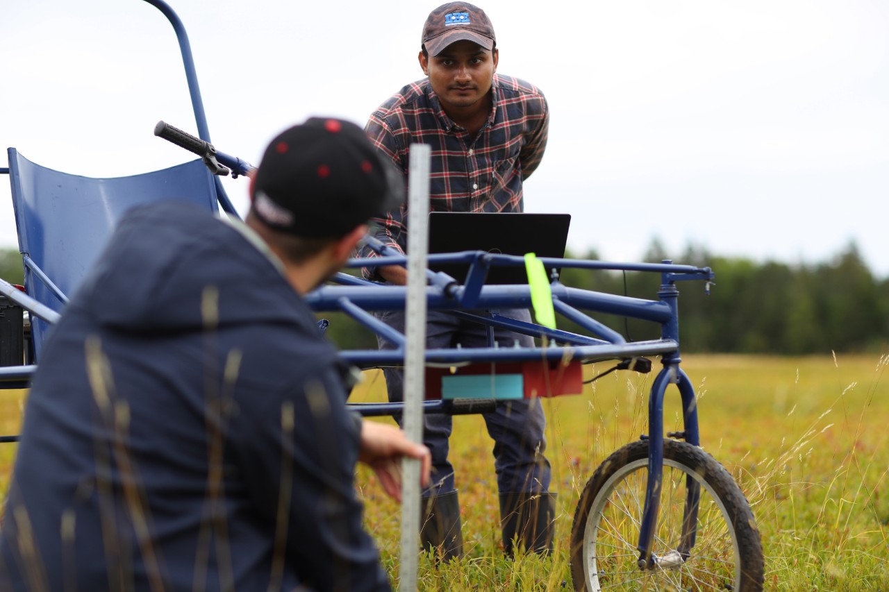 Two people in a field with a piece of agriculture equipment.