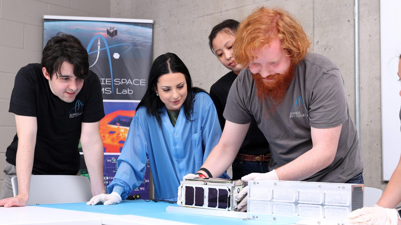 Four people gather around equipment on a table during a presentation.