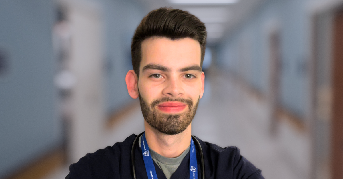 A man with brown hair and a beard stands in a hospital hallway