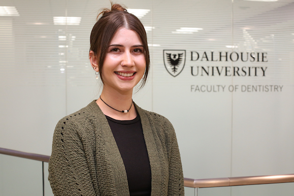 A young woman wearing a green sweater and black shit stands in front of glass wall