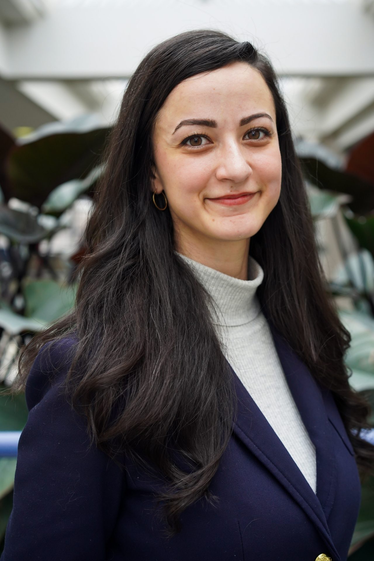 A woman with long black hair wearing a blue blazer and grey shirt