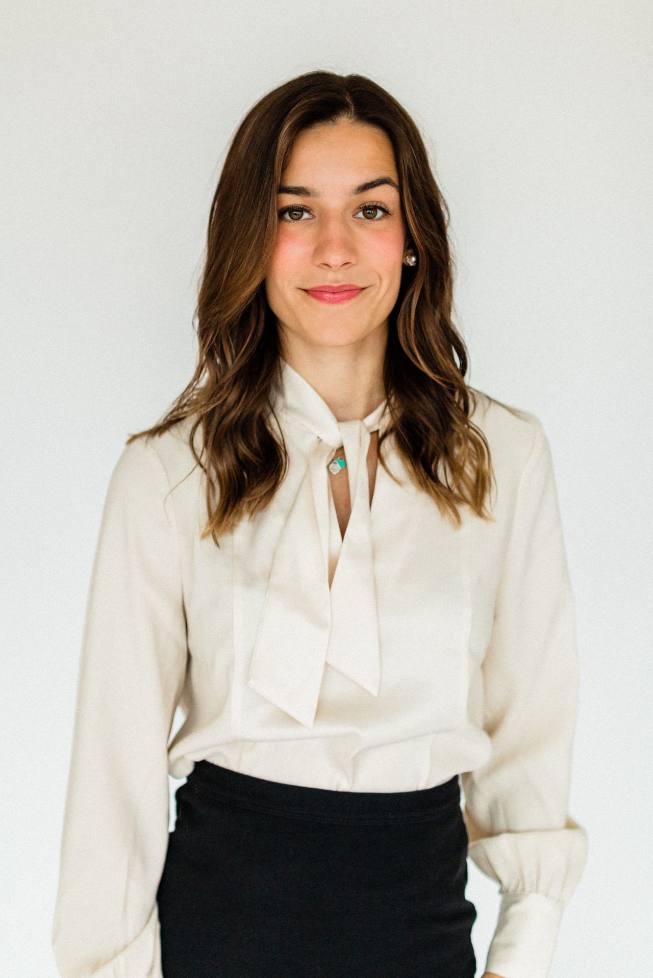 A woman with shoulder length brown hair wearing an ivory blouse and black skirt
