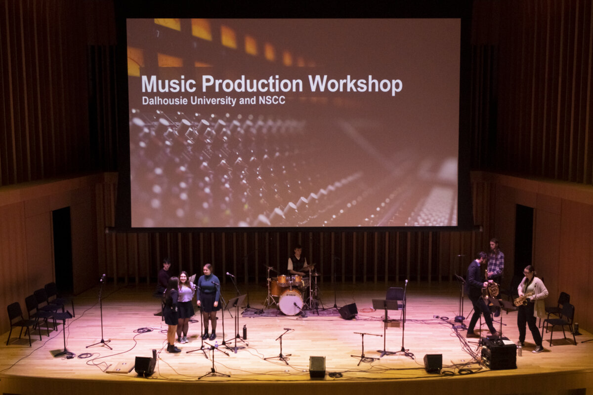 Student performers on stage with a screen reading Music Production Workshop